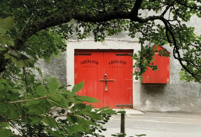 Red double doors labeled 'ABERDOUR' on a grey building, framed by green leaves.