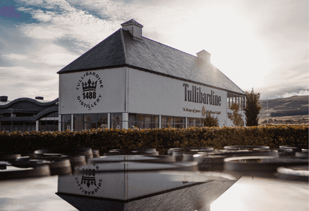 Tullibardine distillery building with crown logo reflected in dark water under bright sunlight.