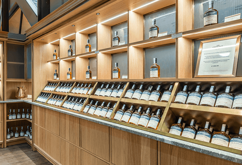 Rows of whiskey bottles displayed on well-lit wooden shelves in a modern retail store.
