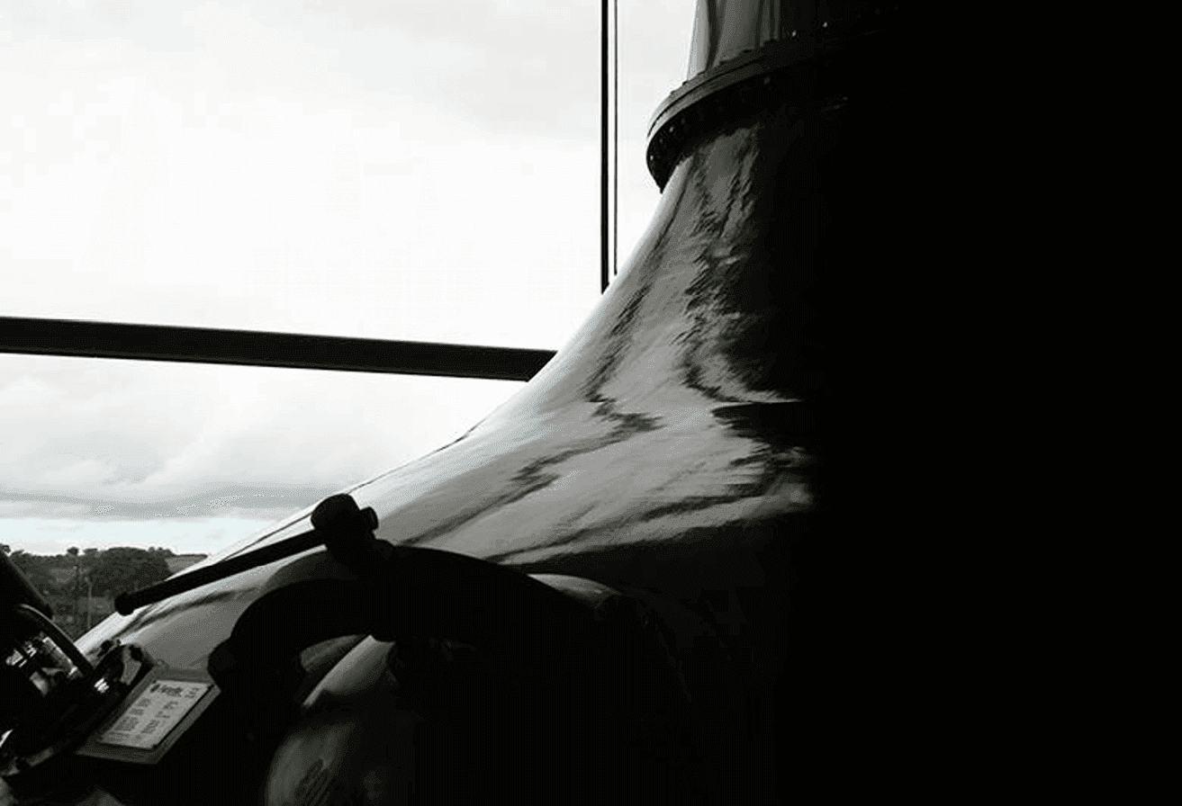 A dark, reflective bell-shaped still stands prominently against a bright, cloudy window background.